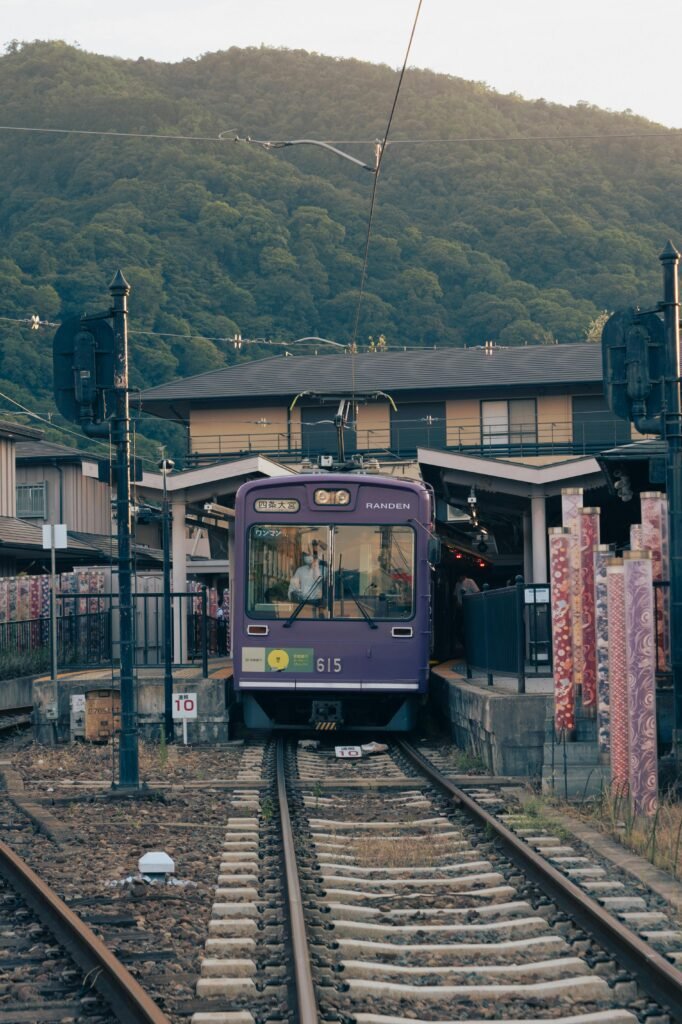 A classic tram approaches Arashiyama Station in Kyoto, Japan against a scenic mountain backdrop.